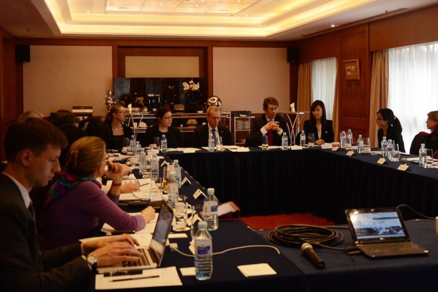 An image of a conference meeting with many attendees sitting around a square conference table.